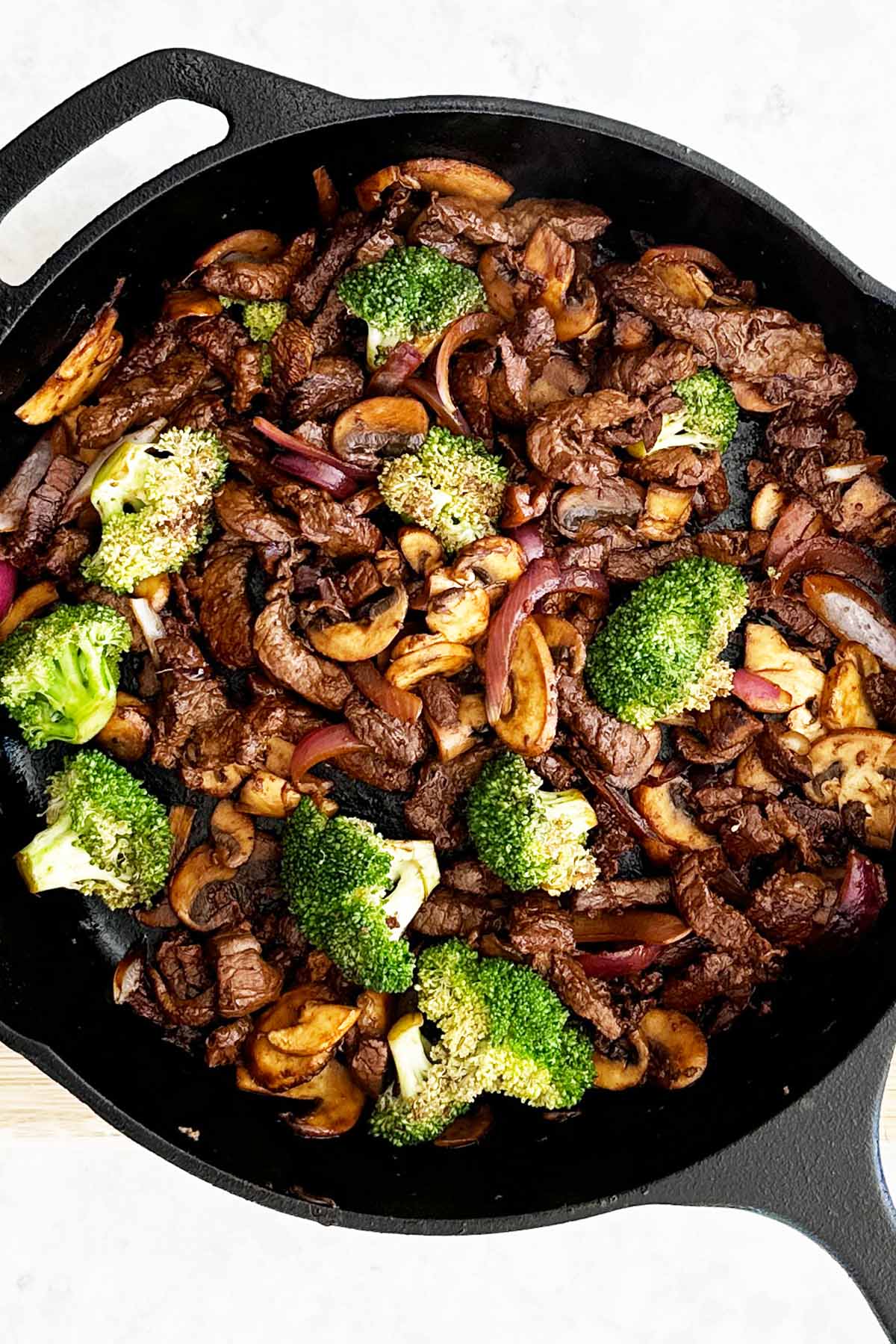 Stir-fried beef, broccoli, onions, and mushrooms in a cast iron skillet, vibrant and lightly caramelised.