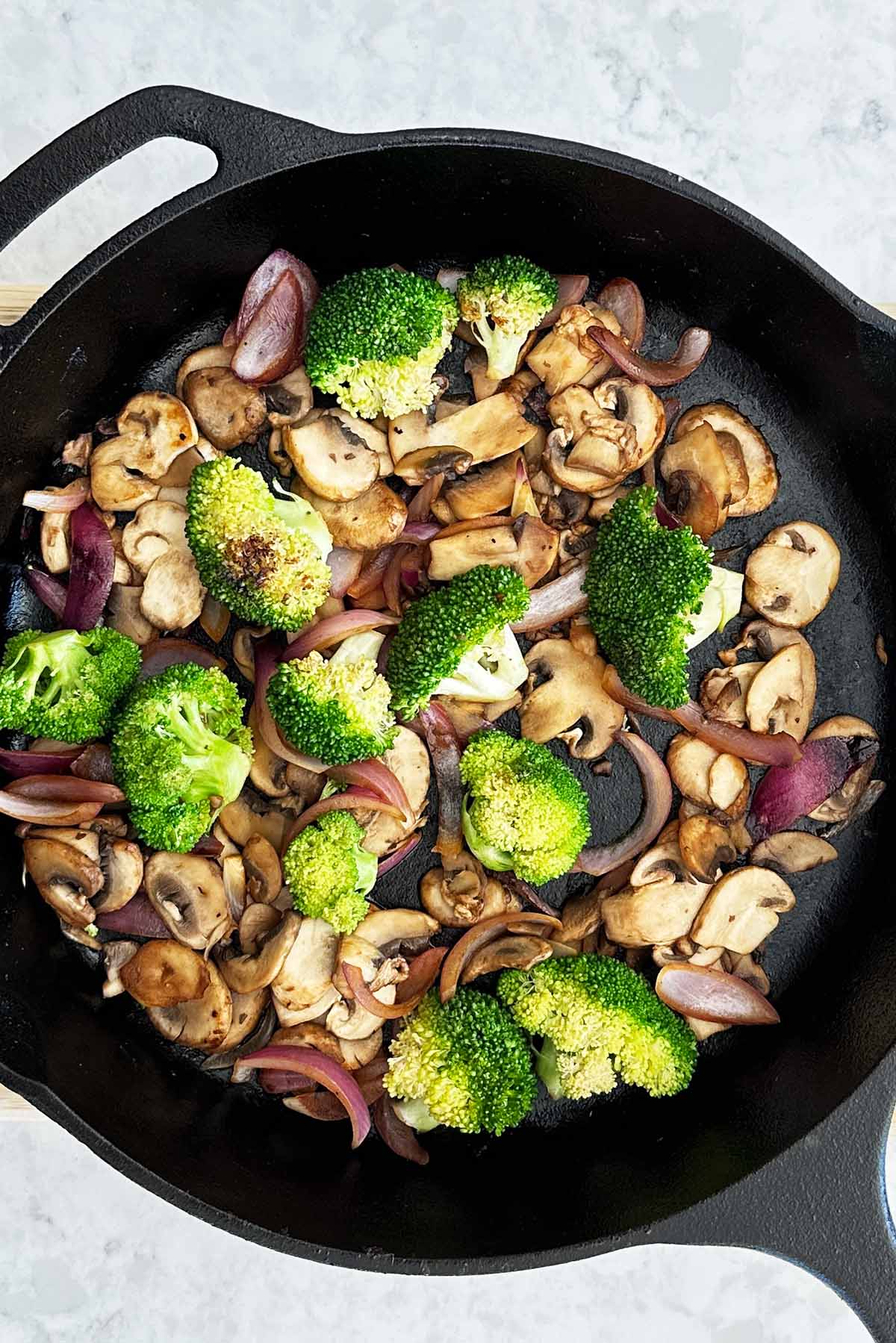 Stir-fried broccoli, onions, and mushrooms in a cast iron skillet, vibrant and lightly caramelised.