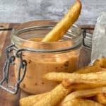 Chili mayo in a glass container with golden crispy chips on a wooden board.