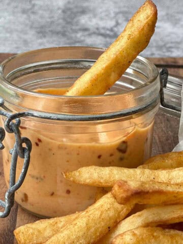 Chili mayo in a glass container with golden crispy chips on a wooden board.