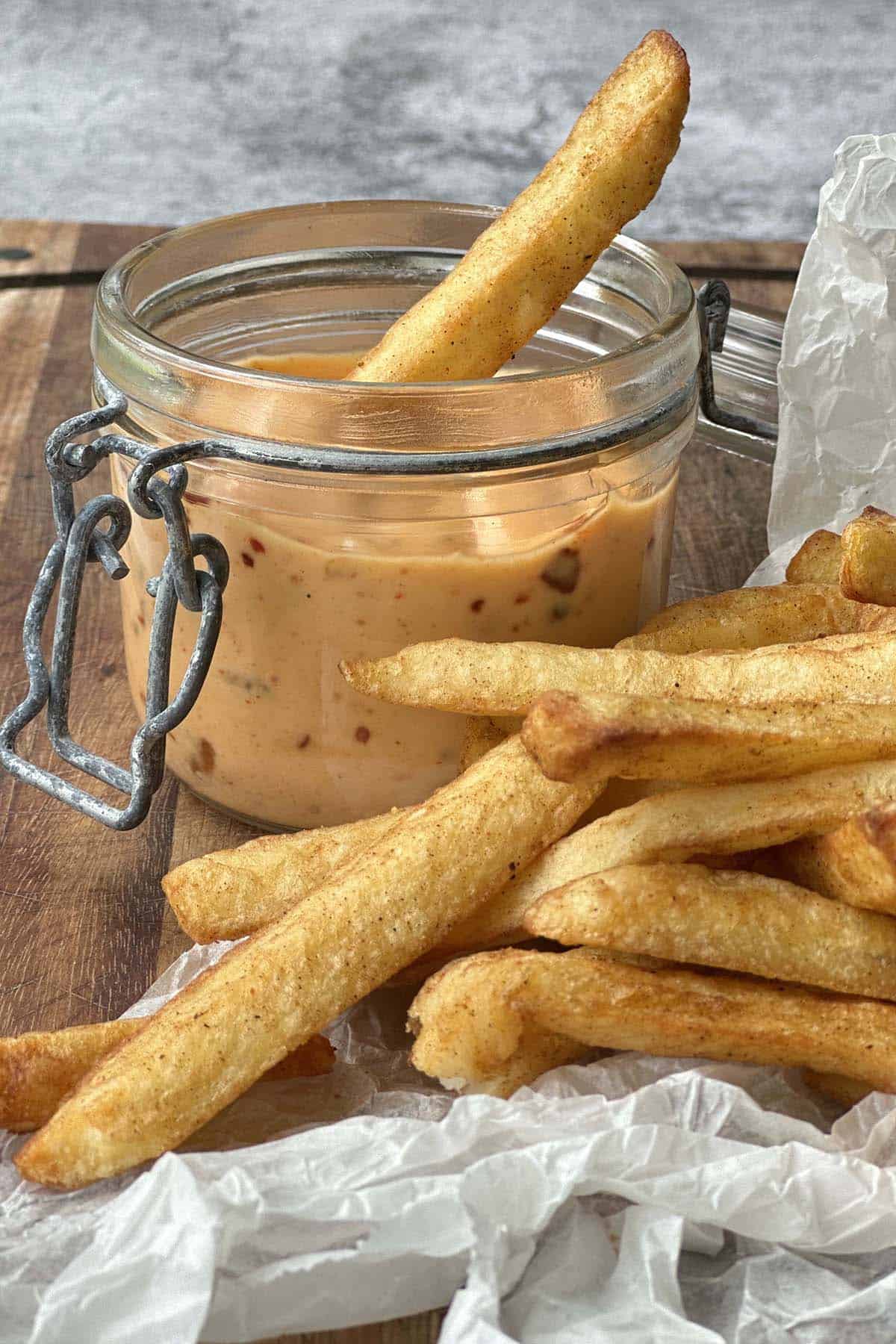 Chili mayo in a glass container with golden crispy chips on a wooden board and a chip dipped into Mayonnaise chili.