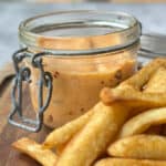 Chili mayo in a glass container with golden crispy chips on a wooden board.