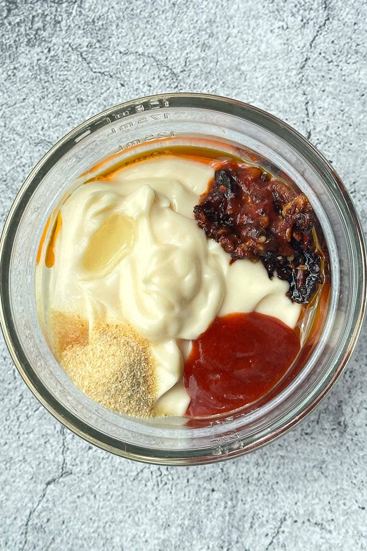 All the ingredients for the Chili aioli added to a glass bowl, each ingredient still visible before mixing.