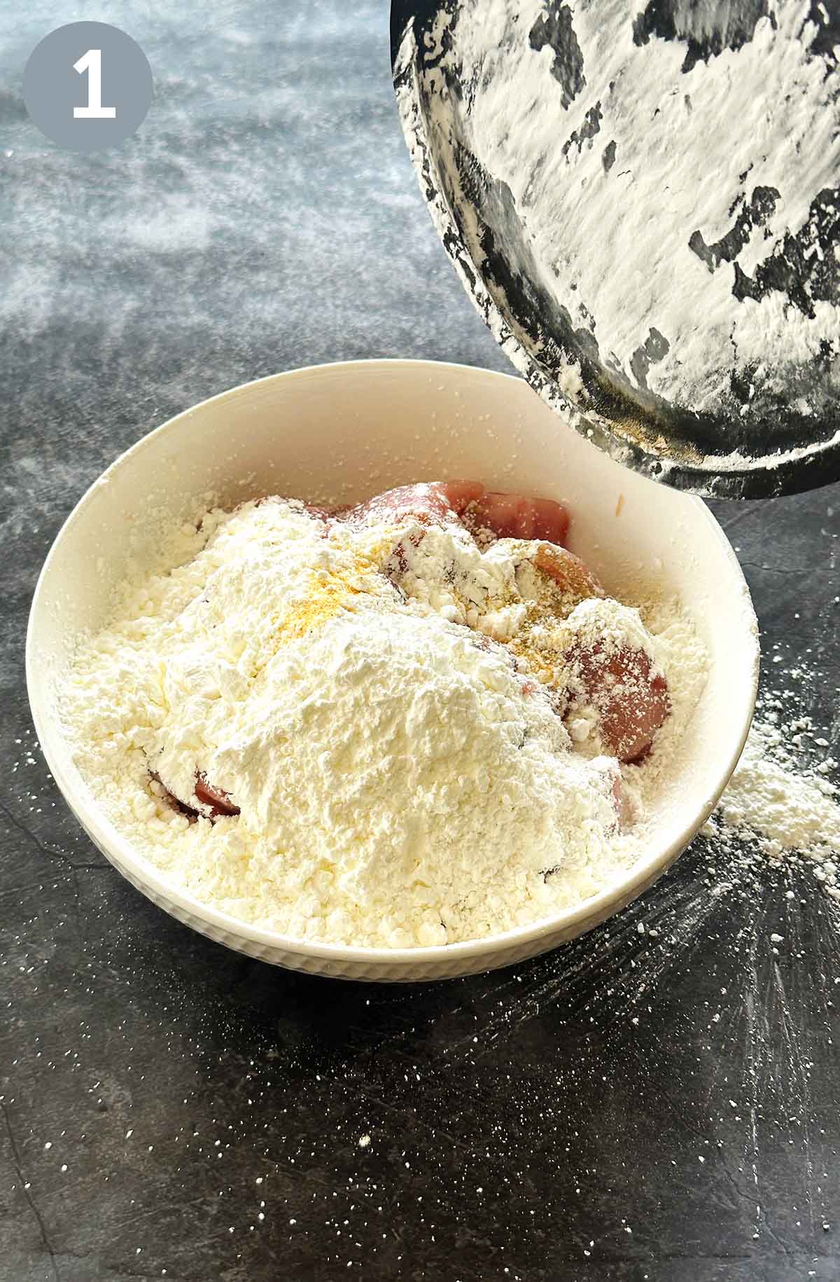 Chicken pieces being tossed in a bowl with a cornflour mixture, ensuring an even coating for a crispy finish.