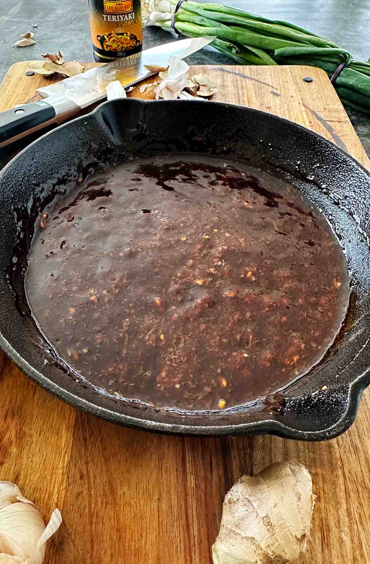 Thick, sticky dark brown teriyaki sauce in a black cast iron skillet, ready to coat crispy fried chicken pieces.