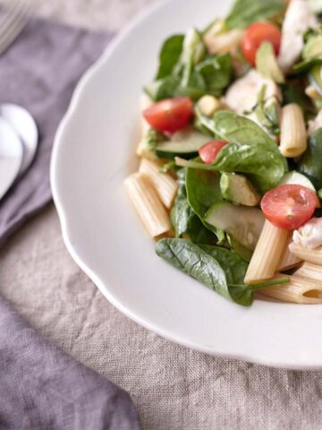 A colourful plate of chicken, pasta, spinach, cherry tomatoes, avocado, cucumber and fresh herbs