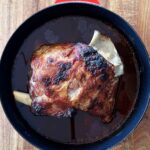 Black deep skillet with slow-braised lamb shoulder, well caramelised and just out of the oven.