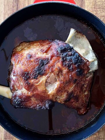 Black deep skillet with slow-braised lamb shoulder, well caramelised and just out of the oven.