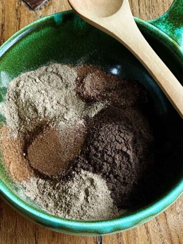 All the spices measured and added to a green bowl with a wooden spoon on edge.