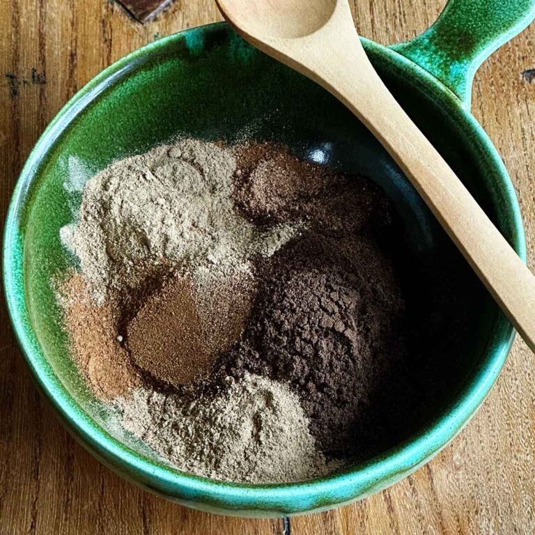 All the spices measured and added to a green bowl with a wooden spoon on edge.