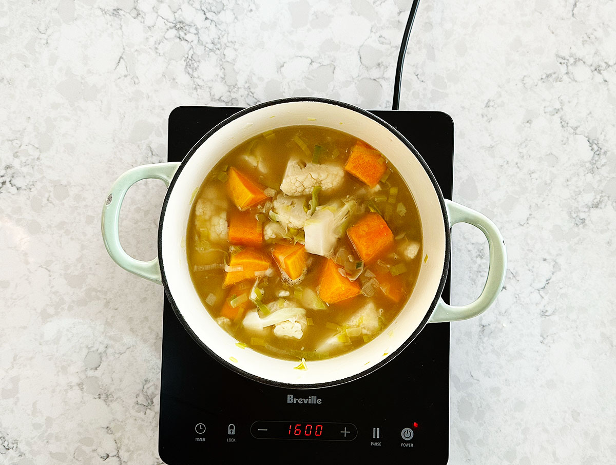 Vegetable stock just added to pot with pumpkin, cauliflower, and aromatics for simmering soup.