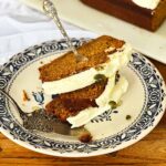 Three slices of moist pumpkin bread with cream cheese frosting on a hearts and flowers plate with silver cutlery.