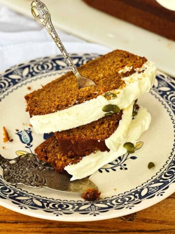 Three slices of moist pumpkin bread with cream cheese frosting on a hearts and flowers plate with silver cutlery.