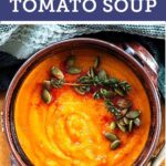 A rustic bowl of pumpkin, carrot and tomato soup garnish with pepitas, thyme and paprika.