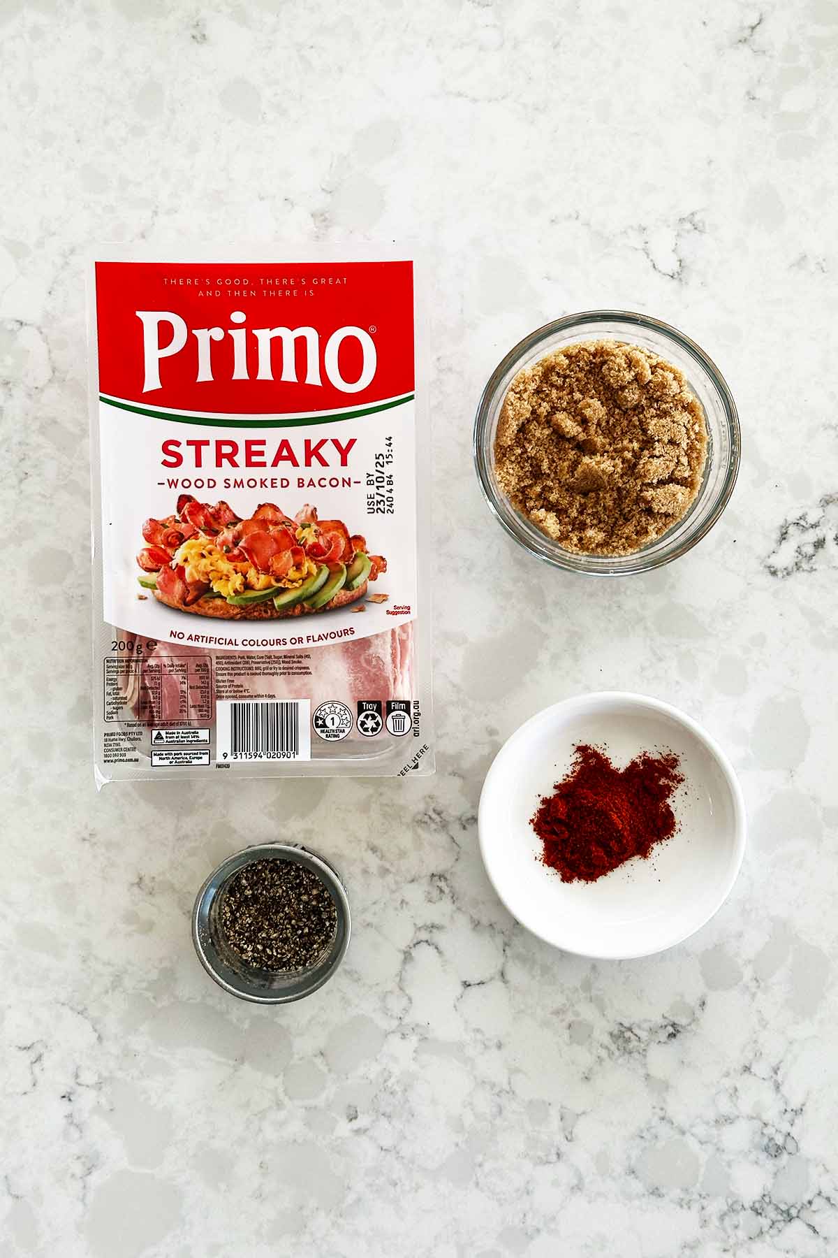 Candied bacon recipe ingredients - bacon, paprika and black pepper on white kitchen bench.