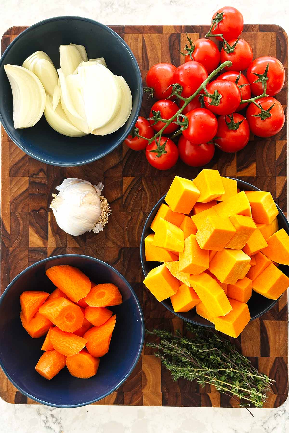 Fresh prepped ingredients for roasted butternut squash and tomato soup, including pumpkin, onion, carrots, garlic bulb, and thyme.