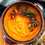 A rustic bowl of pumpkin, carrot and tomato soup garnish with pepitas, thyme and paprika.