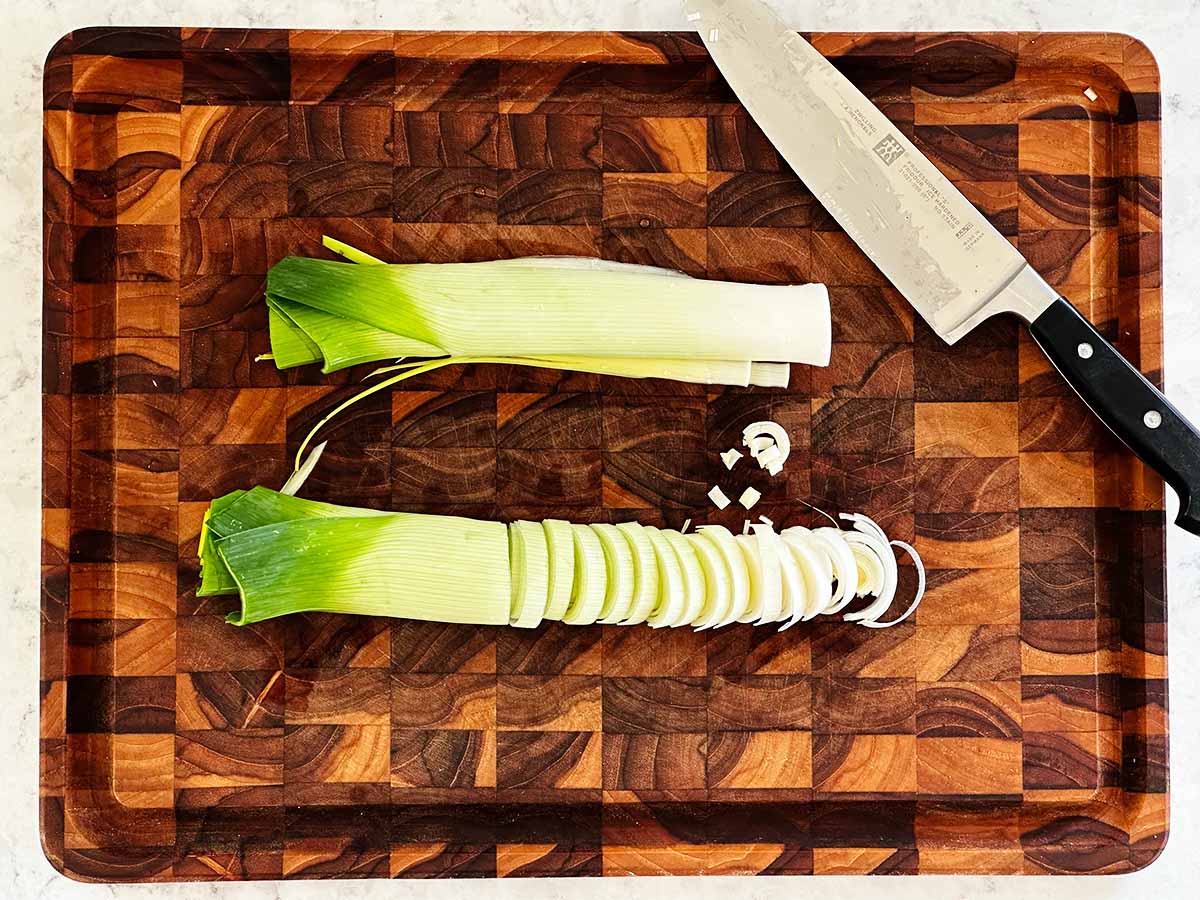 Two halves of a leek, one of which has been sliced and the other half on a cutting board with a knife on the side