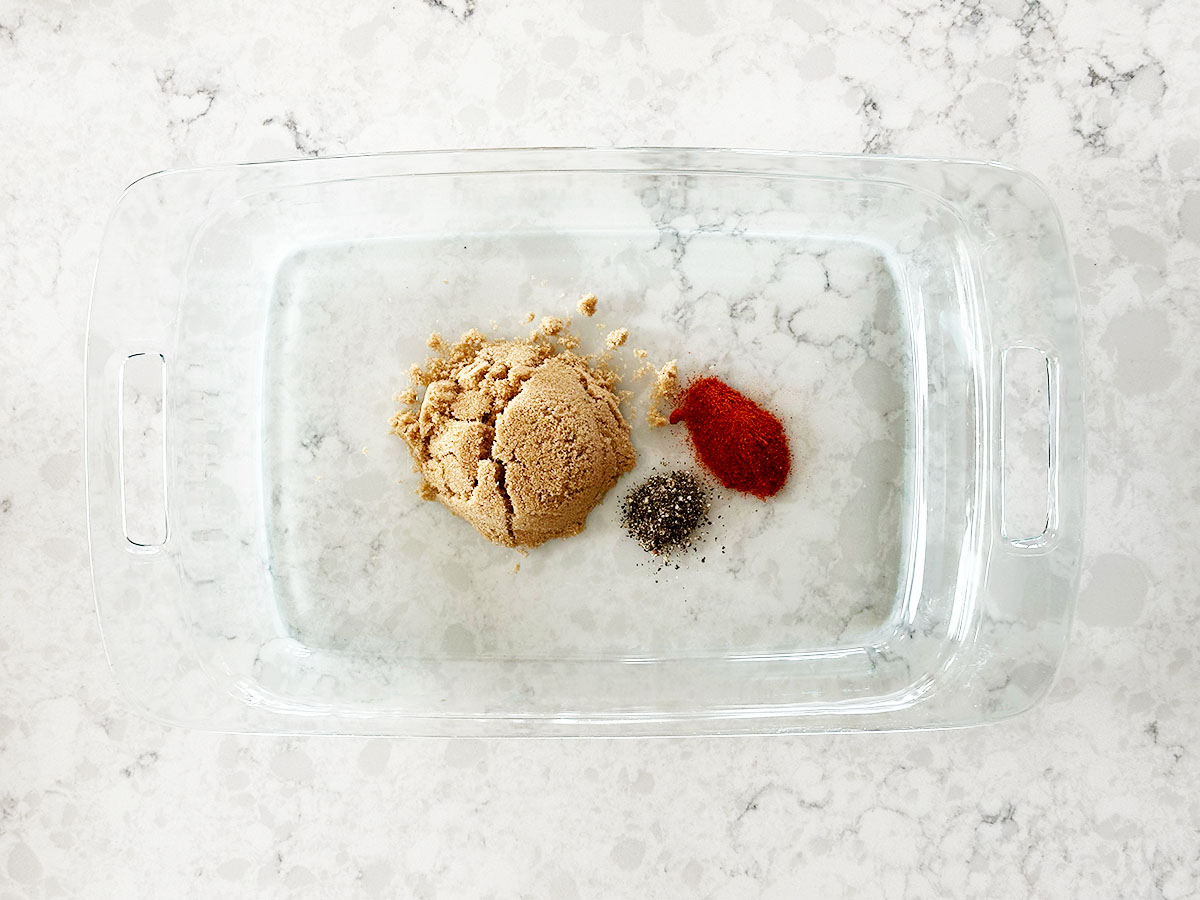 Brown sugar, paprika, and pepper measured in glass tray for candied bacon.