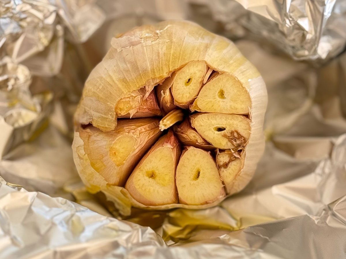 Whole garlic bulb with top cut off, drizzled with olive oil, and wrapped in foil ready for roasting.