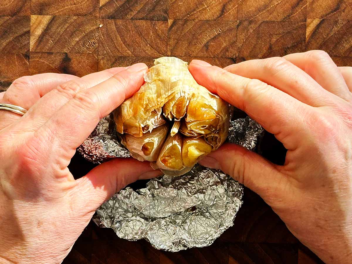 Soft roasted garlic cloves squeezed from a golden bulb after baking, ready to use in soup.