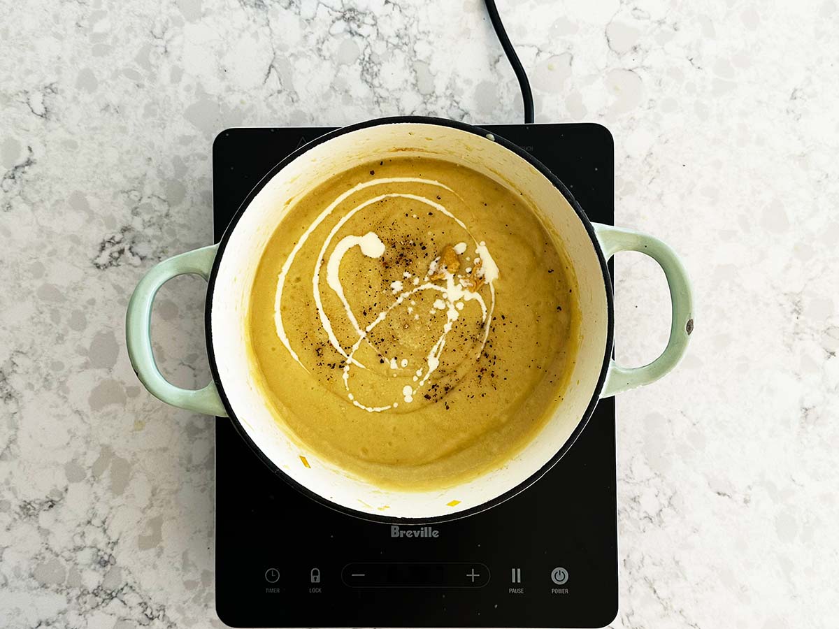 Seasoning creamy potato, leek and cauliflower soup with salt, pepper, and Dijon mustard and cream.