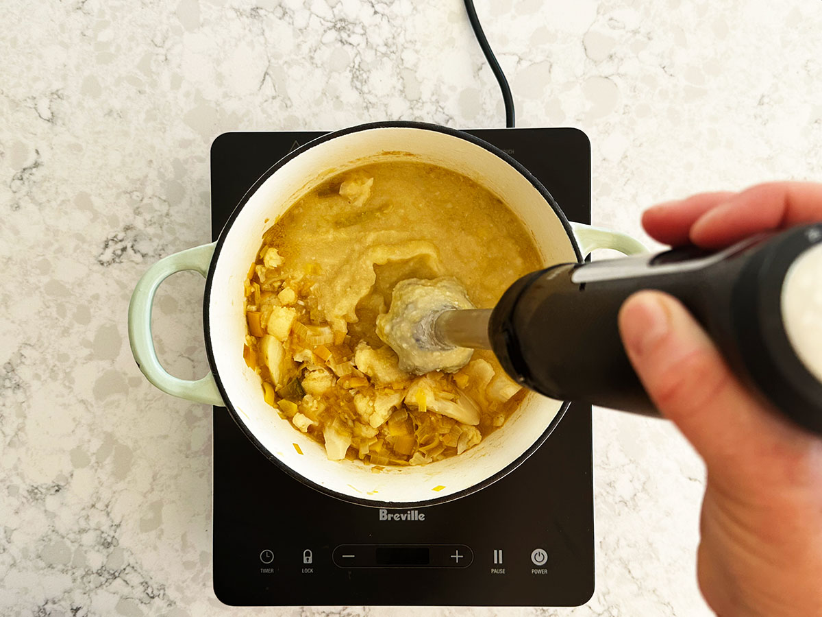 Immersion blender blending potato, leek and cauliflower soup until silky smooth in the pot.