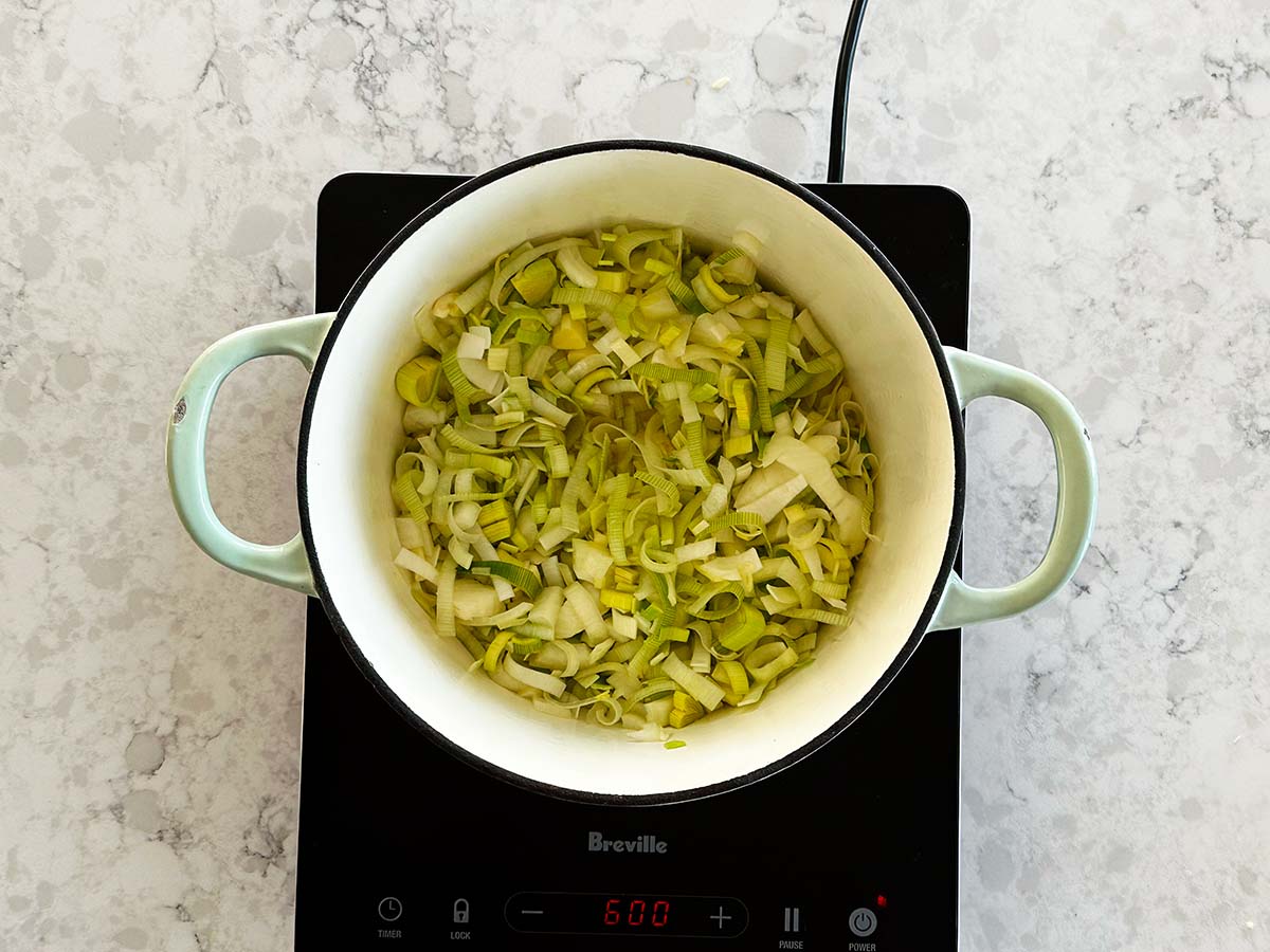 Leeks, onion, and garlic sautéing in butter in a large pot for potato, leek and cauliflower soup.