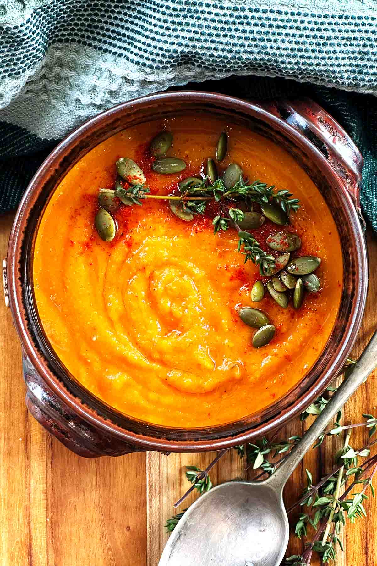 A rustic bowl of pumpkin, carrot and tomato soup garnish with pepitas, thyme and paprika.