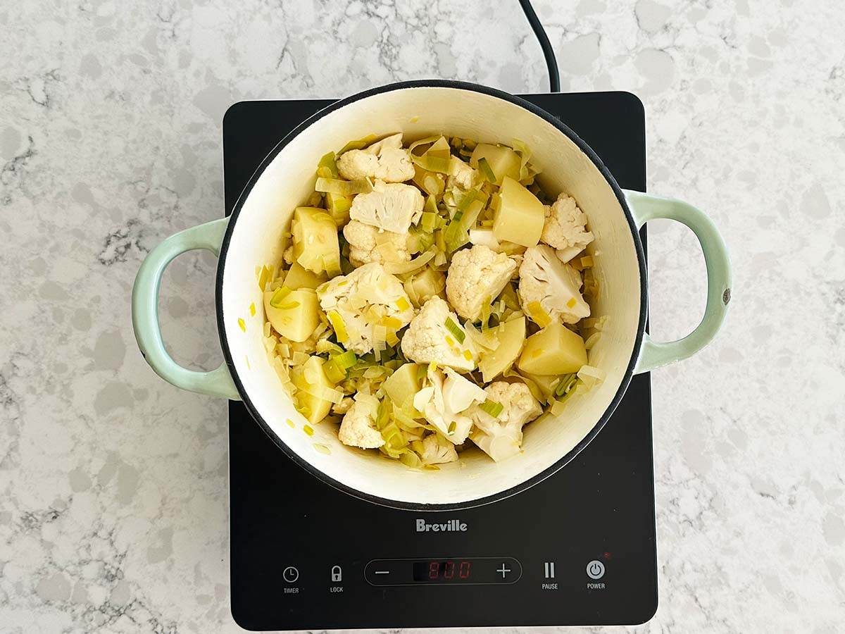 Potatoes and cauliflower added into sautéed leek and onion mixture in a pot.