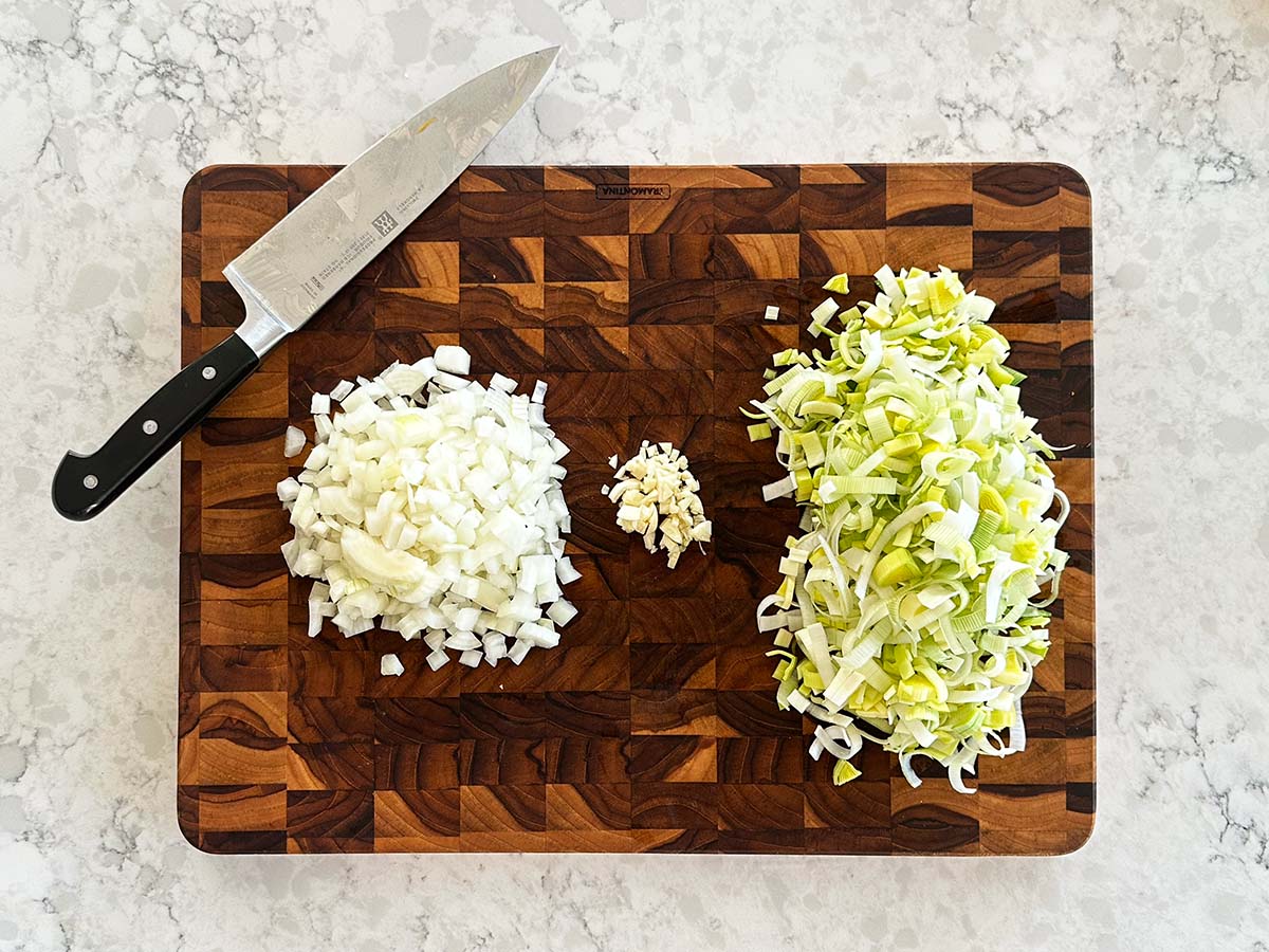 Diced onion, sliced leek, and minced garlic arranged on a chopping board before cooking soup.