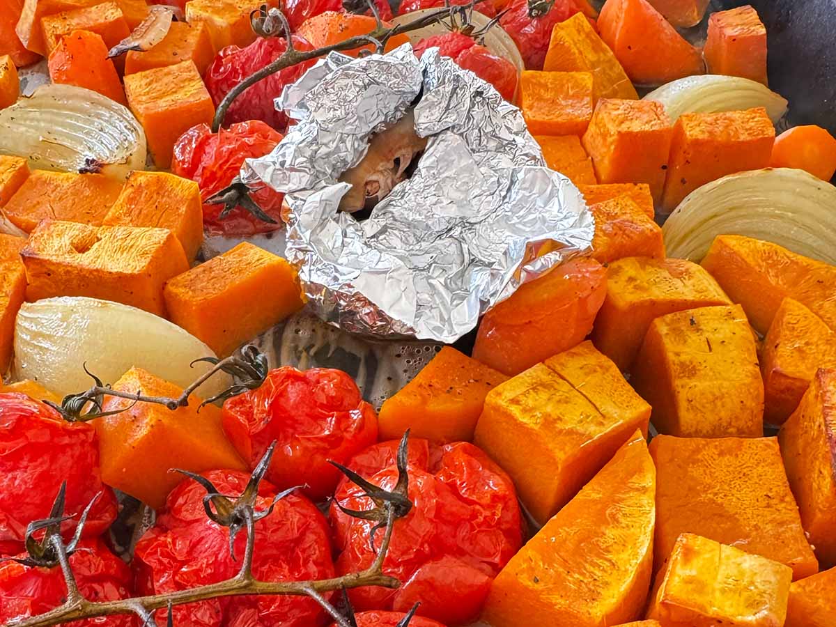 Butternut squash, tomatoes, carrots, onion, and thyme arranged on a baking tray, seasoned and drizzled with olive oil, ready for roasting.