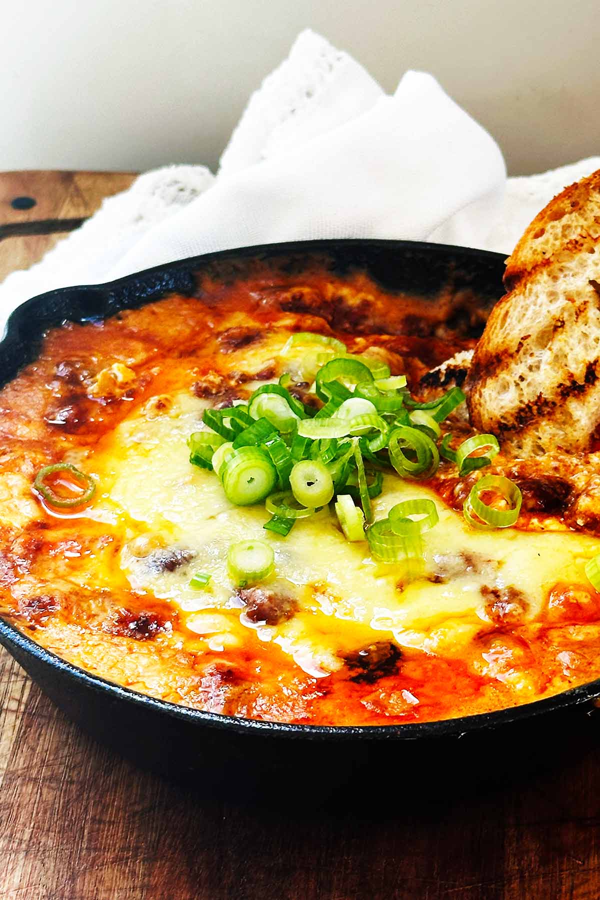 Baked chili cream cheese dip in a cast iron skillet, golden and bubbly, with a piece of crusty bread dipped into the warm, cheesy center.