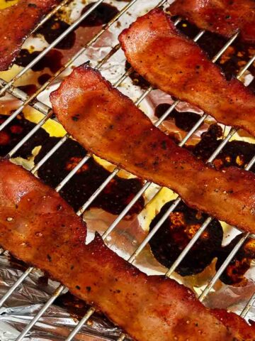 Candied streaky bacon on roasting rack on a foil lined baking sheet.