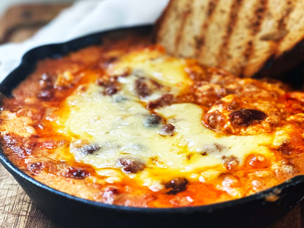 Baked chili cream cheese dip golden and bubbly in skillet with toasted bread on side.