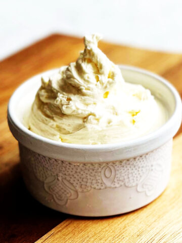 Whipped cream in a white ramekin on a wooden surface.