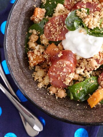Chorizo pumpkin with couscous and spinach salad in a bowl with dollop of yogurt