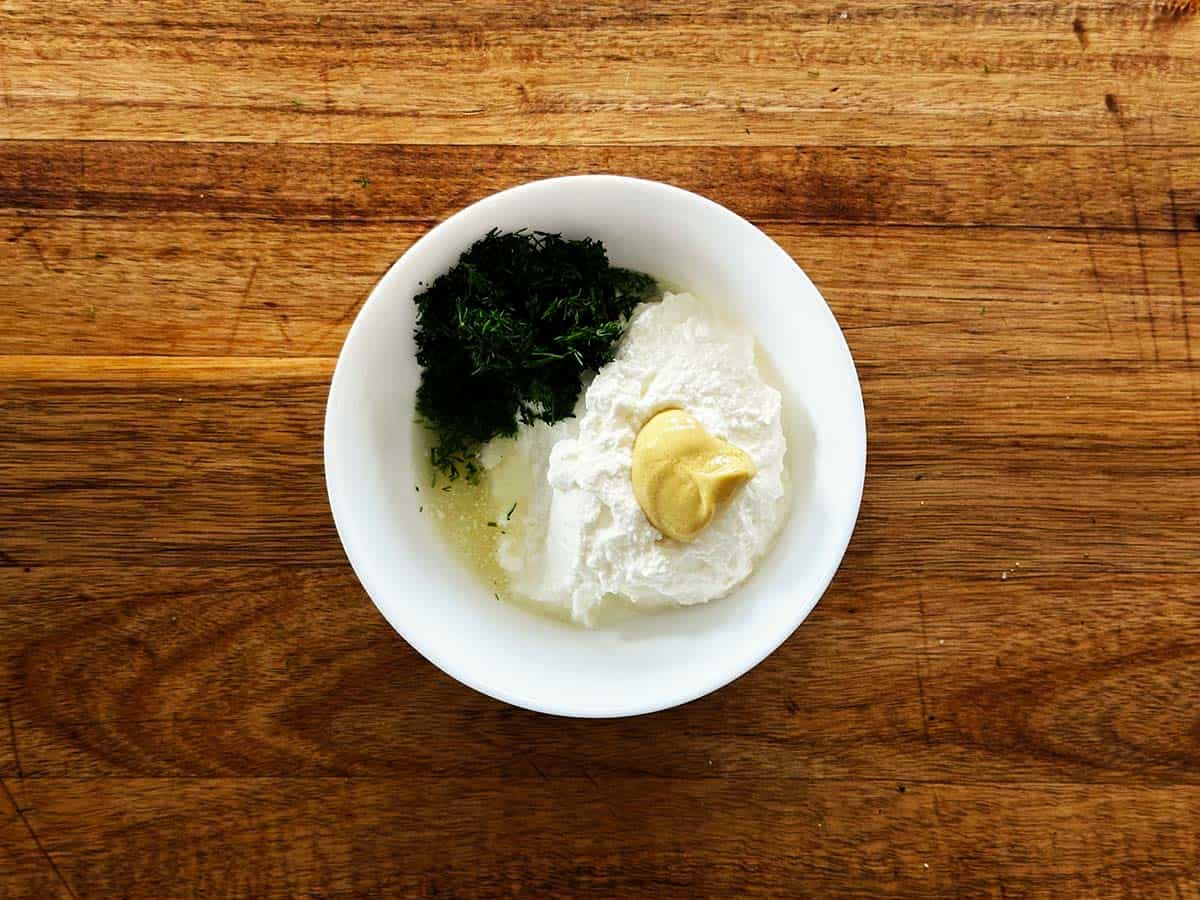 Greek yoghurt, lemon, dill and Dijon mustard being added to a bowl for dill yoghurt sauce.