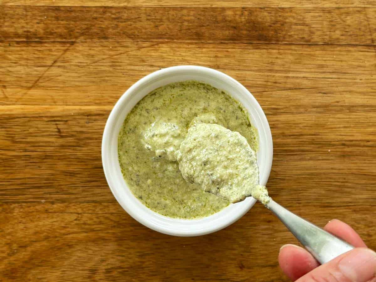 Add water to creamy pesto dressing in a bowl to thin the sauce.