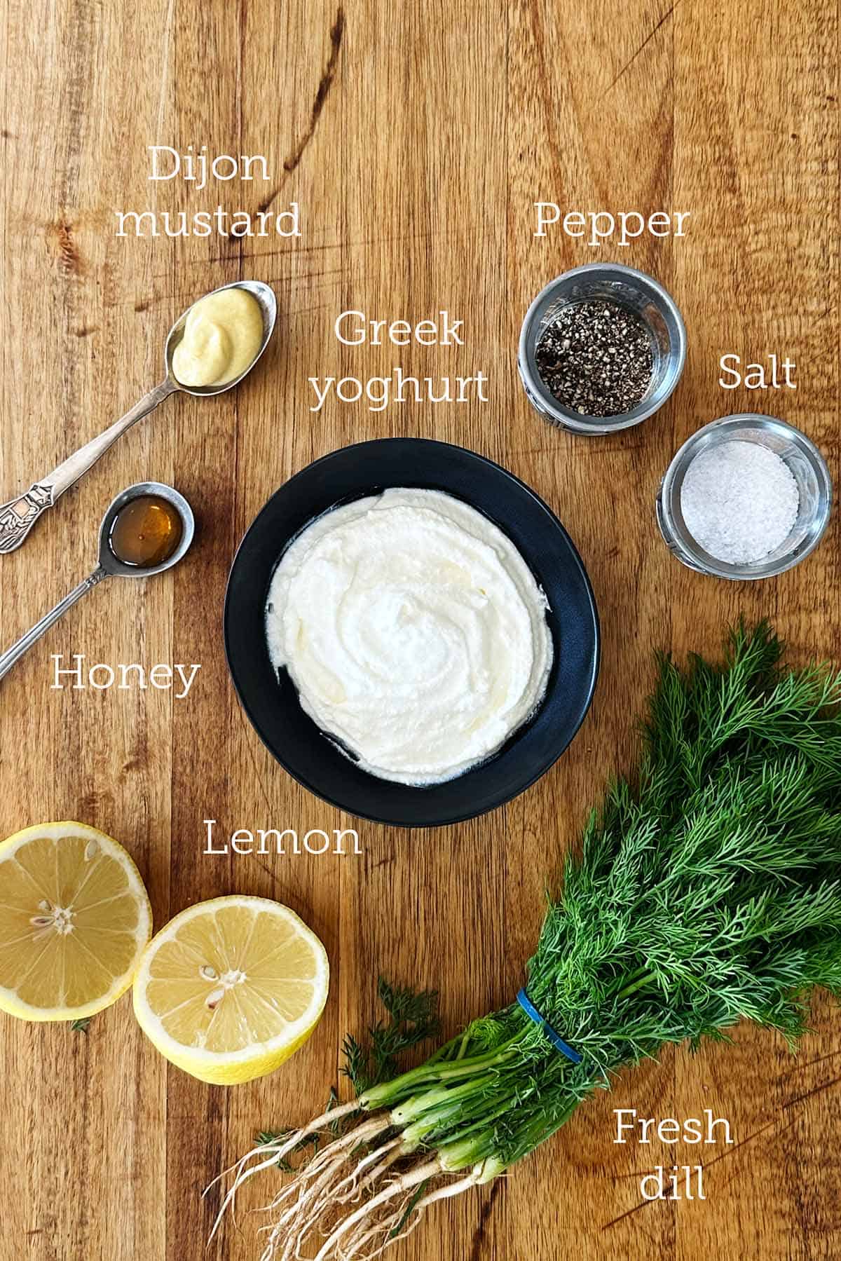 Greek yoghurt, lemon, fresh dill, honey and Dijon mustard on wooden board.