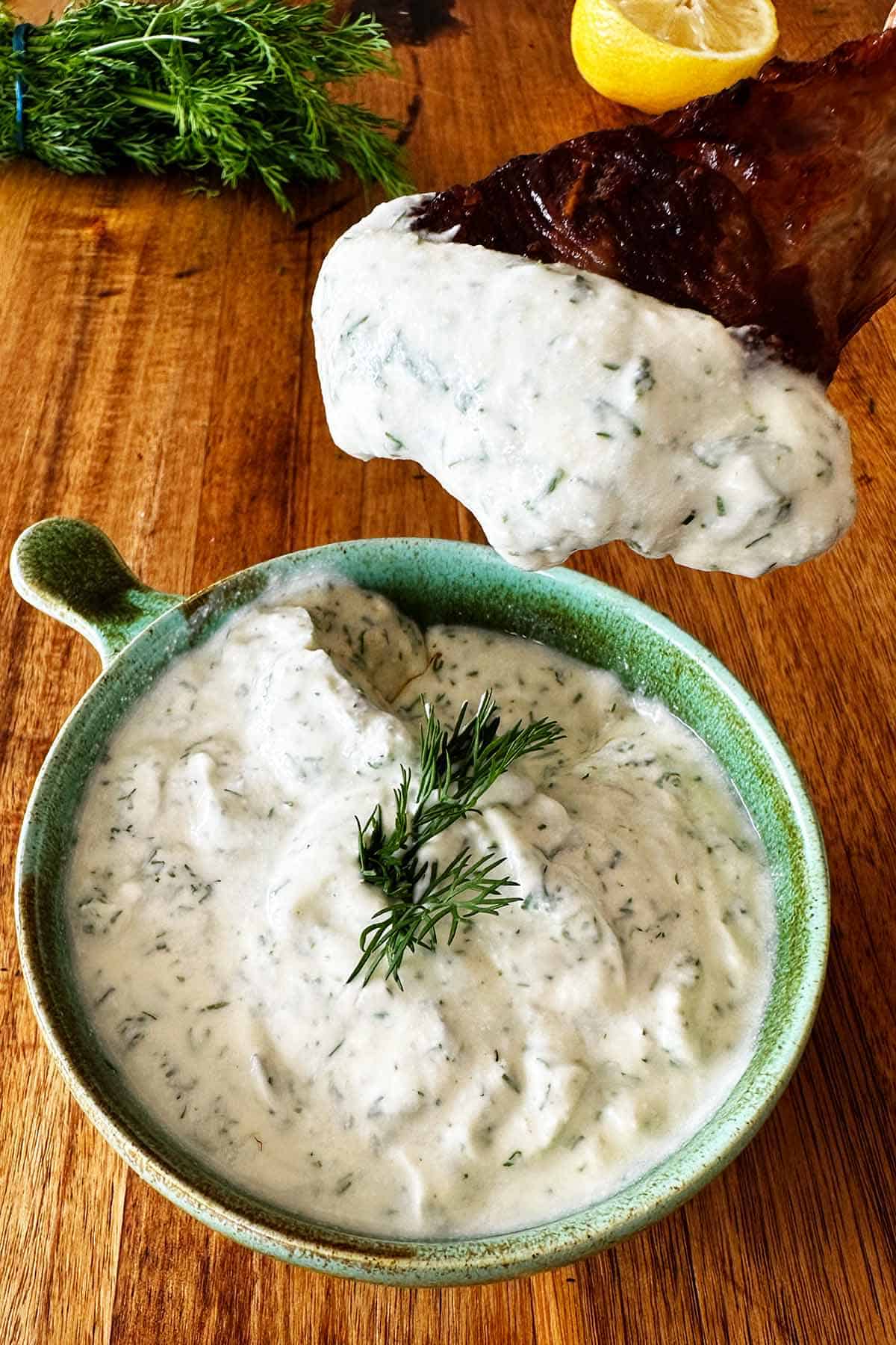 Lamb chop being dipped into a bowl of creamy dill yoghurt sauce