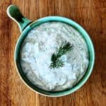 Dill lemon yoghurt sauce in a green bowl, garnished with fresh dill, on a wooden board