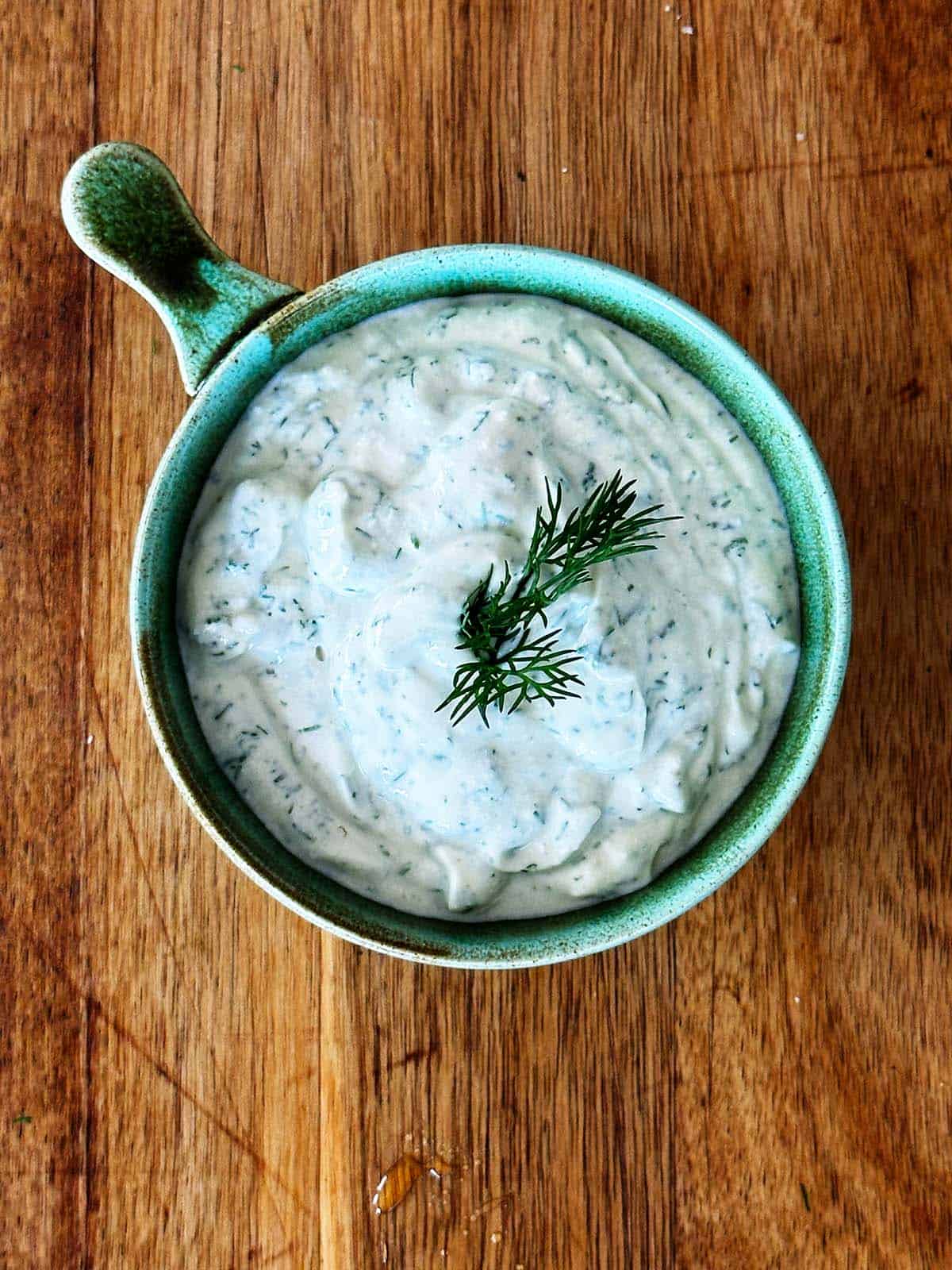 Dill lemon yoghurt sauce in a green bowl, garnished with fresh dill, on a wooden board