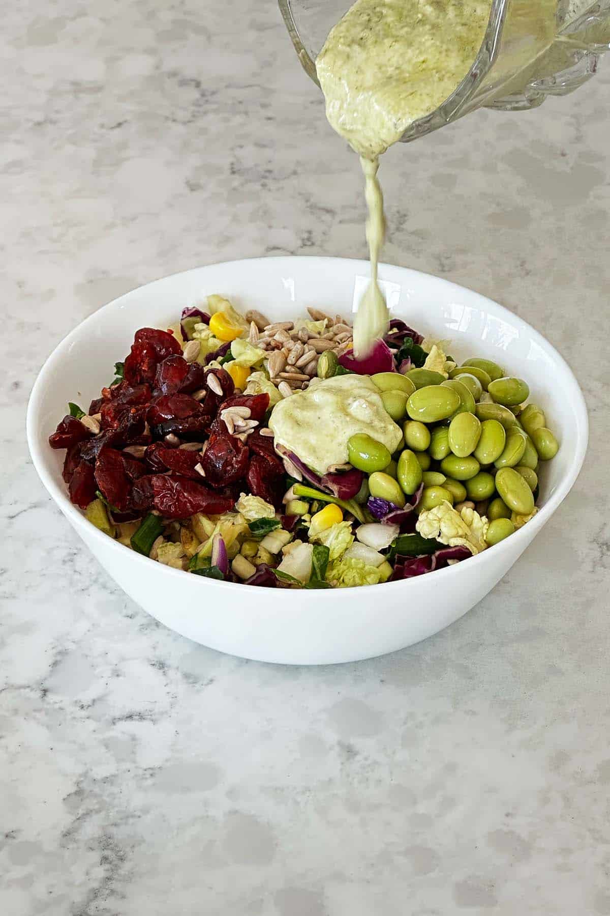 Fresh vegetable salad with creamy pesto yoghurt dressing pouring over ingredients.