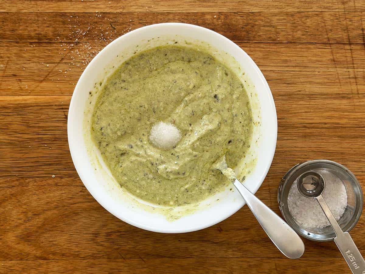 Creamy pesto dressing in a bowl with salt being added and ready to be stirred in.