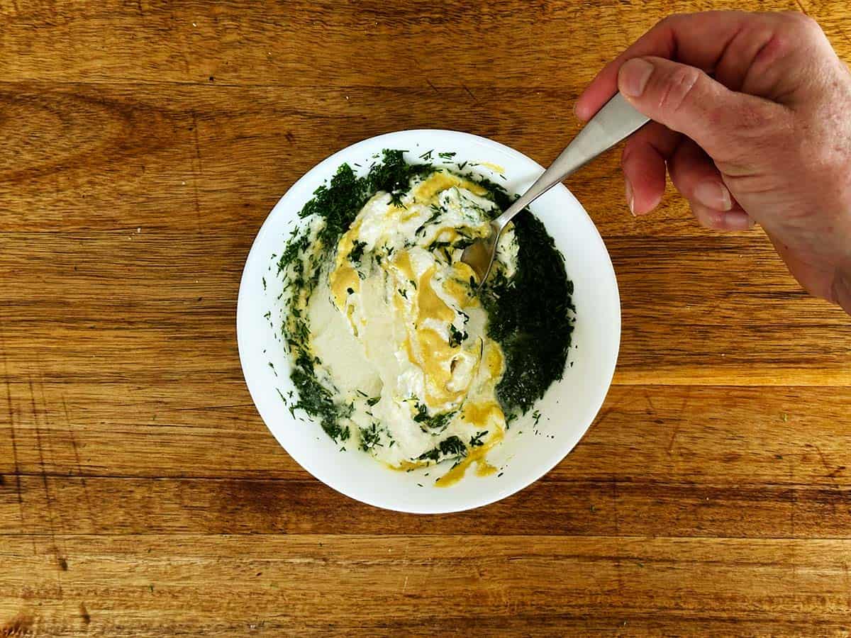 Greek yoghurt, lemon, dill and Dijon mustard being stirred with a spoon in a bowl