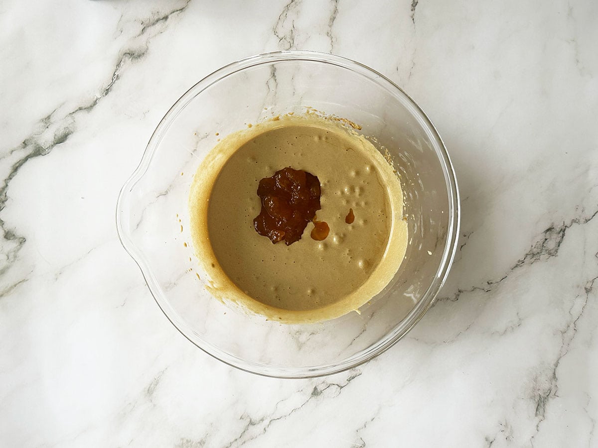 Adding apricot jam to Malva pudding batter in glass bowl