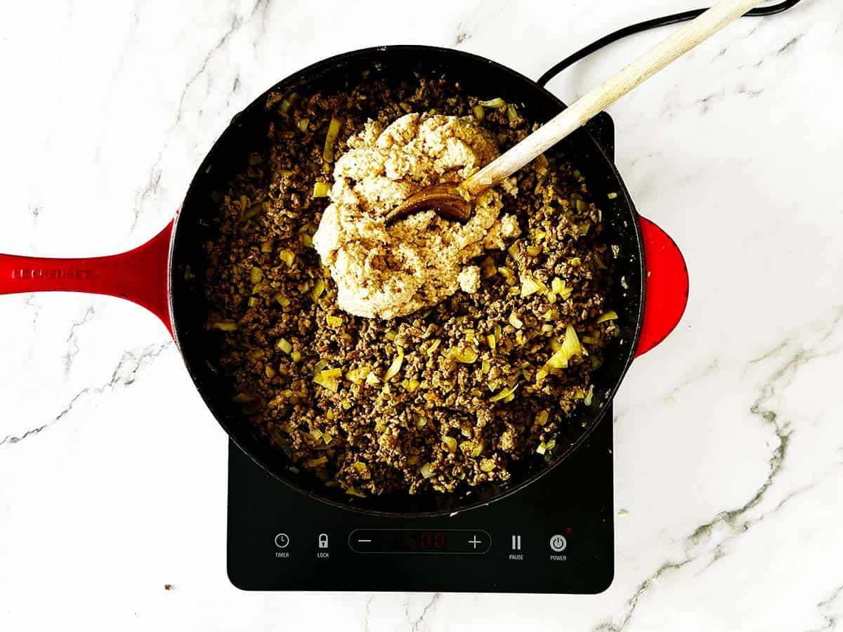 Breadcrumb mixture being added to seasoned mince in skillet