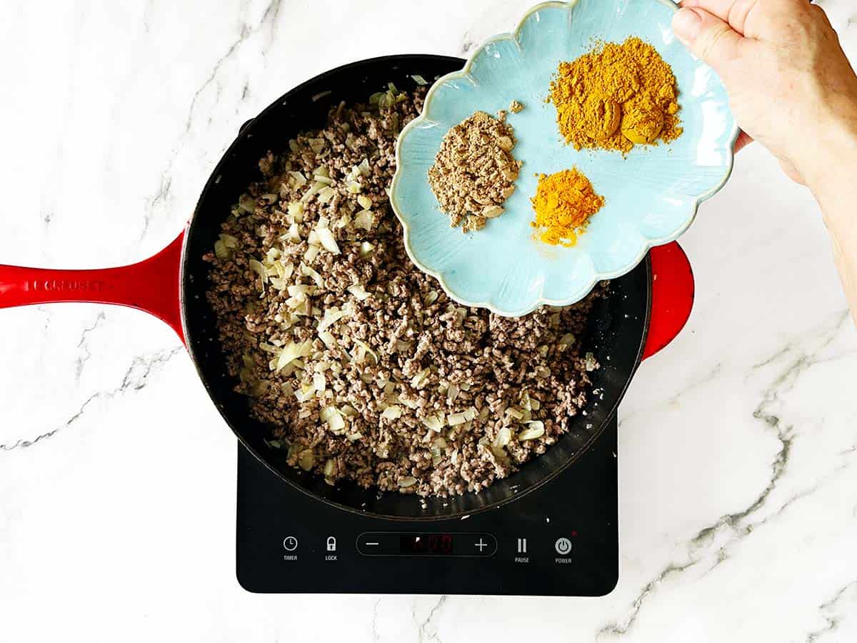 Adding turmeric coriander and curry powder to mince mixture in skillet