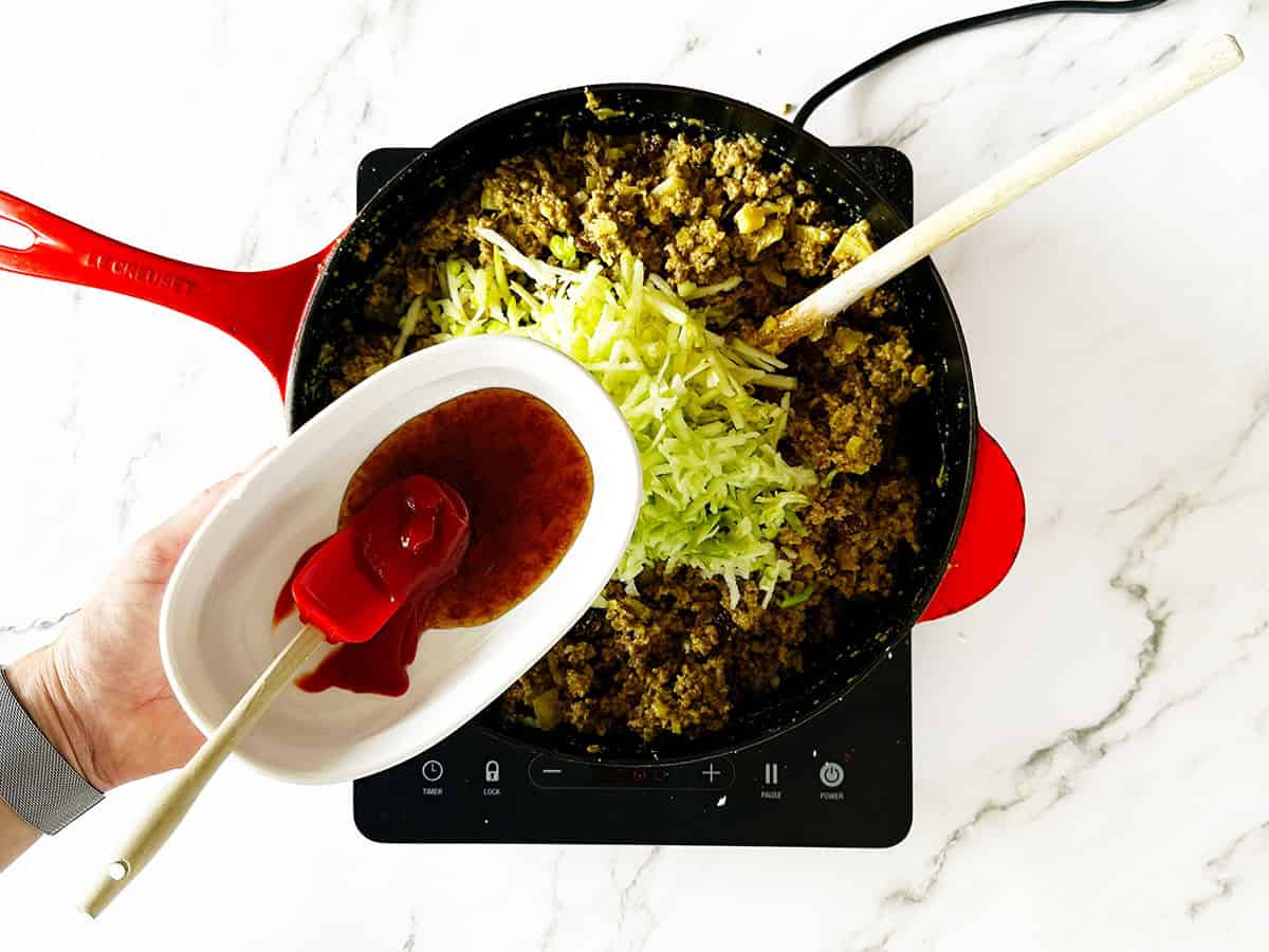 Grated apple, tomato sauce and chutney added to mince mixture in skillet